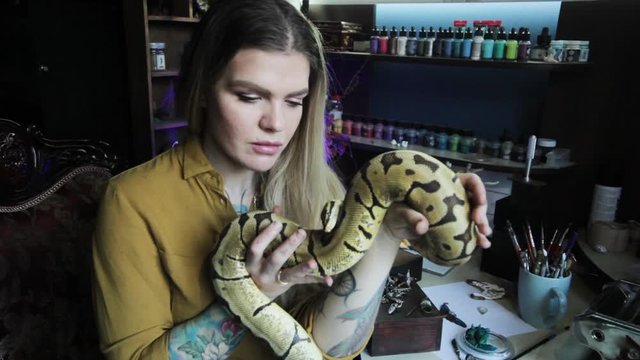 Woman jeweler holding a snake in her hands. She plays with the snake while resting.