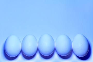 Five chicken eggs vertically at the bottom of the frame with a directed in the center of the entire frame of blue tones.