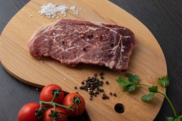 Raw beef steak with spices on a dark board. View from above.
