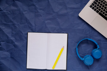 laptop, notebook, pencil and headphones on a blue background, copy space