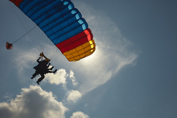 Detail of a canopy of a parachute and silhouettes of an instructor and a passenger during a tandem jump against a blue sky with clouds, close-up. Parachute jumping.
