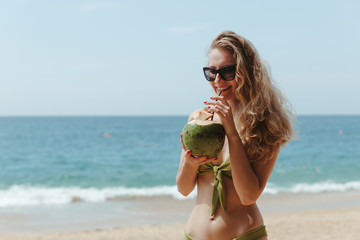The girl with the coconut on the beach. Girl drinks coconut milk on the beach. High quality photo