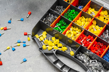 Tips of various sizes and colors for crimping multi-core electrical wires. Wire tips in a box on a grey concrete background