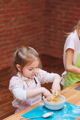 Little girls kneading the dough for baking the cake. Kids taking part in baking workshop. Baking classes for children,  aspiring little chefs. Learning to cook. Combining and stirring ingredients