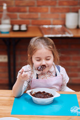 Little girl smelling the melted chocolate and cocoa. Kid taking part in baking workshop. Baking...