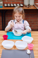 Happy, smiling little girl stirring the yolk with sugar. Kid taking part in baking workshop. Baking classes for children, aspiring little chefs. Learning to cook. Combining and stirring ingredients