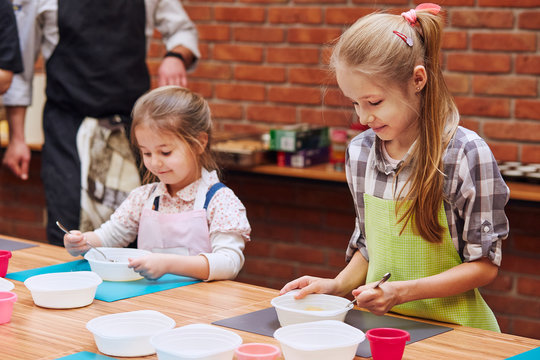 Little girls stirring the yolk with sugar. Kids taking part in baking workshop. Baking classes for children,  aspiring little chefs. Girls learning to cook. Combining and stirring prepared ingredients