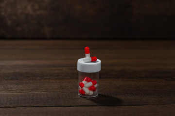 Red-white capsule pills in a jar on a wooden background. Global health concept.