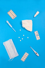 Antiviral drugs with a medical mask, syringes and a thermometer on a blue background. Vertical orientation, top view.
