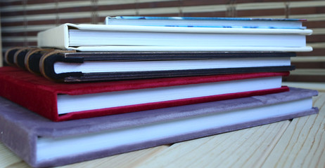 stack of photo books and albums in multi-colored covers on a wooden table, close-up