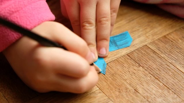 Closeup of the hands and fingers of a 4 year old caucasian child girl drawing on a little church cut out of paper on parquet floor at home. Seen in Germany in March