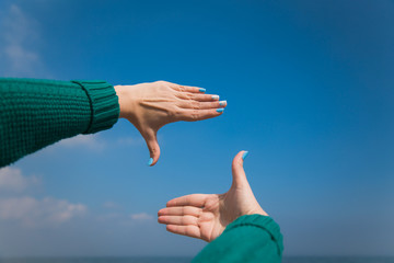 Close up of female caucasian hands isolated at blue sea and sky background. Young woman forms frame with her two hands as if looking at something virtual and invisible in distance. Point of view shot.
