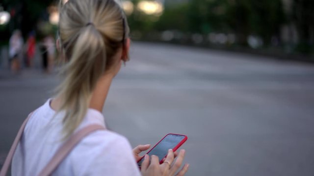 Positive smiling female traveller spending time in downtown and searching information about location of hotel via smartphone device hailing with hand for stop taxi cab on road