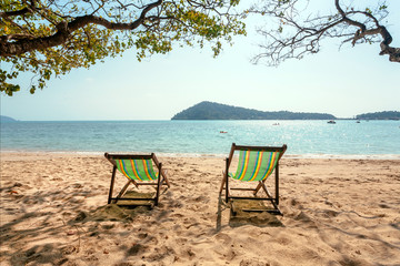 Sunny tropical island scene with beach lounges on sand. Happy day of tourists with swimming and deck chair near an ocean