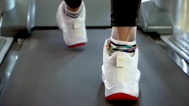 Closeup athletic feet running on treadmill in fitness gym. Back view of black shoes having workout on treadmill. Low view sneakers training in sport club.