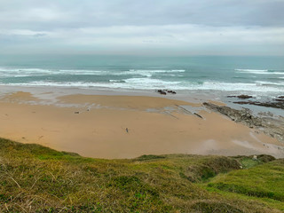 Paisaje de costa con playa, mar y vegetación, con dos personas paseando con una mascota. Costa Vasca.