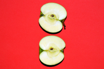 Two halves of a green juicy sliced ​​apple on red background