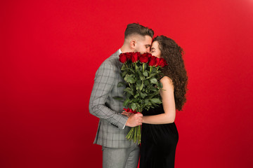 Romantic couple with rose bouquet kissing isolated on red background