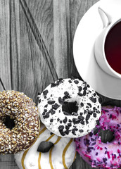 bright doughnuts in pink, white and brown and a white Cup of tea close-up on a black and white background are placed under the text vertical