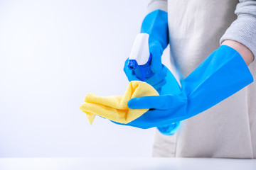 Young woman housekeeper is doing cleaning white table in apron with blue gloves, spray cleaner, wet yellow rag, close up, copy space, blank design concept.