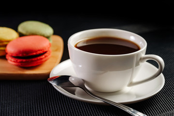 a cup of coffee on a saucer with a spoon and cakes macarons