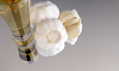 Fototapeta na wymiar Garlic bulbs and garlic cloves on a mirror with a glass of alcohol rakia