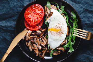 Top view of sandwich with fresh arugula, fried shiitake mushroom, shallot onion, egg served with tomatoes.