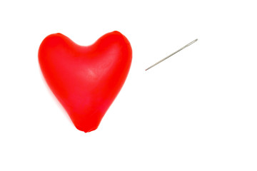 Red heart from a ball with a needle isolated on white background. A red heart from a balloon will be pierced by a sewing needle.