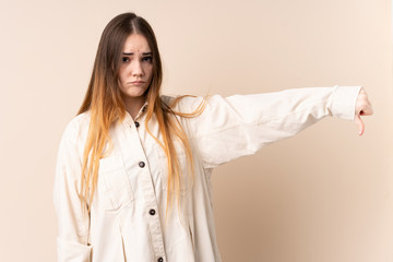 Young caucasian woman isolated on beige background showing thumb down with negative expression