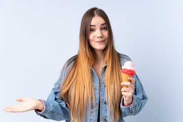 Young woman with a cornet ice cream isolated on blue background making doubts gesture while lifting the shoulders