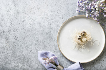 Easter table setting with nest and violet decor on grey stone table. Top view. Space for text.
