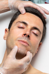 Hands with medical exam gloves inspecting middle aged male face.