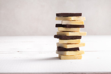 Stack of raw dark bitter chocolate and cocoa butter on old rustic white table with copyspace.