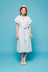 brunette asian girl in striped dress and straw hat on blue background