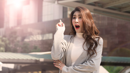 Fototapeta premium Asian business woman standing and finger up like a eureka action and feeling happy which represent have a brilliant idea, thoughtful, solve problem, imagination, inspiration or clever moment in work