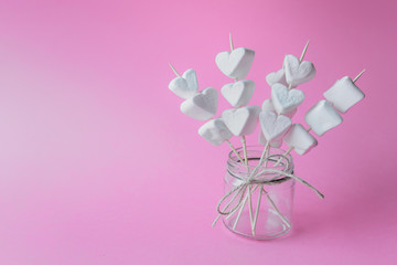 Sweet decoration with heart shaped marshmallows on wooden sticks on pink background. Photo with copy blank space.