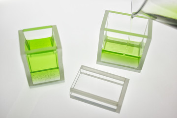 Scientific lab glass cuvette with green transparent liquid on white background.