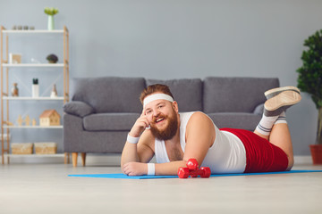 Funny red fat man doing exercises on the floor smiling while lying on the floor at home.