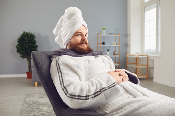 Funny strange fat bearded man in a bathrobe does spa treatments on his face rests in a room