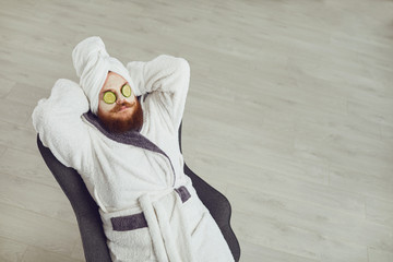 Funny fat bearded man with a cosmetic mask on his face in bathrobe towel on his head on his face...