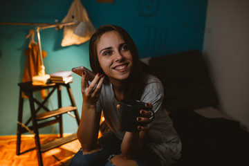 young woman using mobile phone in her room. evening scene