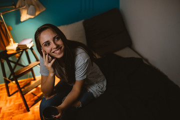 Fototapeta premium young woman using mobile phone in her room. evening scene