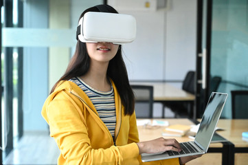 Cropped shot of a young female student wearing a VR glasses and using a laptop.