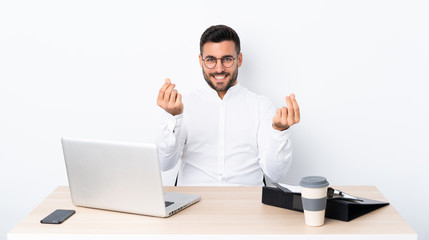 Young businessman in a workplace making money gesture