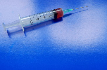 A syringe with medicine and a needle , on a blue background close up. Space for text.