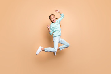 Fototapeta na wymiar Full body profile photo of beautiful funny little lady jumping high up celebrating winning raise fists wear blue sweater jeans footwear isolated beige color background
