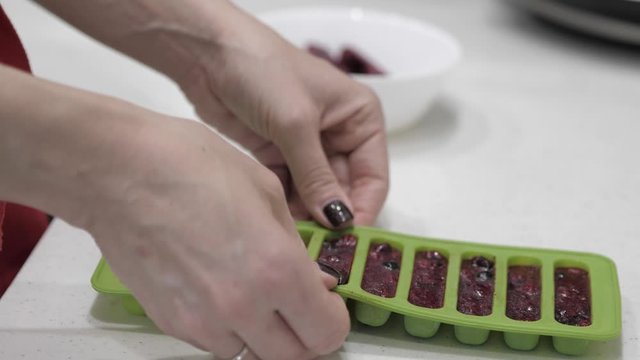 Female hands pull cubes from frozen berries from a green silicone mold and place them in a white cup.