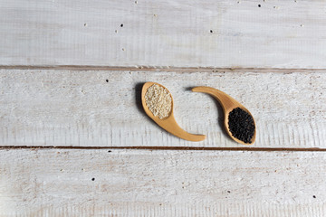 White and black sesame seeds in wooden spoons on white background
