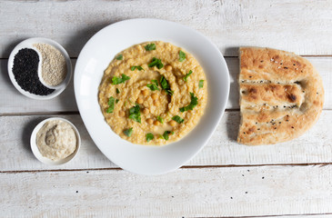 Plate with hummus, bread, tahini, sesame seeds on white wooden background