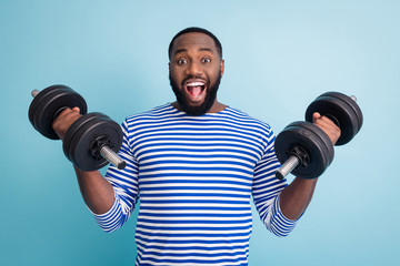 Fototapeta na wymiar Photo of cool funny handsome dark skin guy open mouth lifting two heavy dumbbells weight practicing hard gym strong man wear striped sailor shirt isolated blue color background
